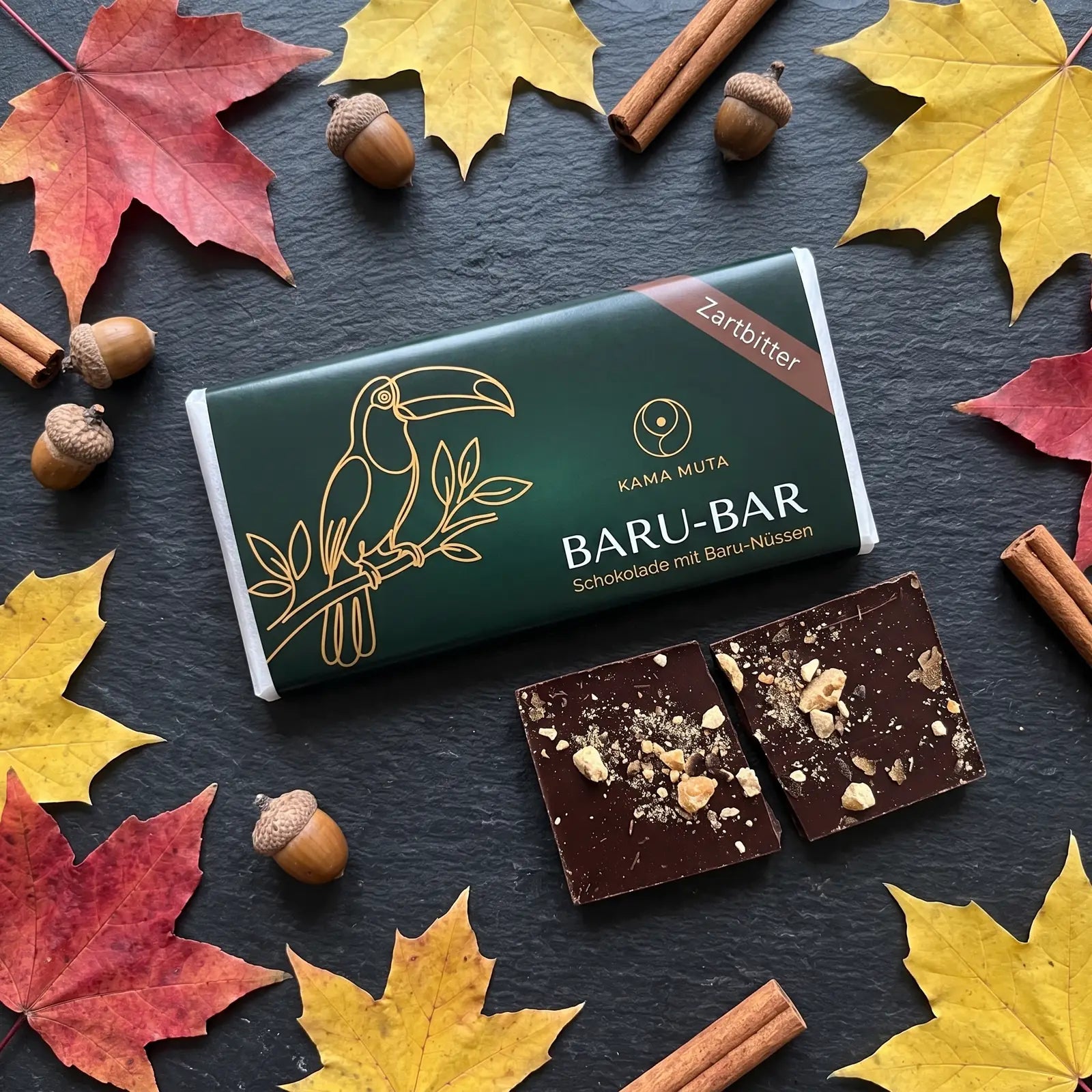 BARU-BAR Zartbitter auf dunklem Schiefer mit Herbstlaub, Eicheln und Zimtstangen, davor zwei Stücke Zartbitterschokolade mit gehackten Baru-Nüssen (KI-generiert)
