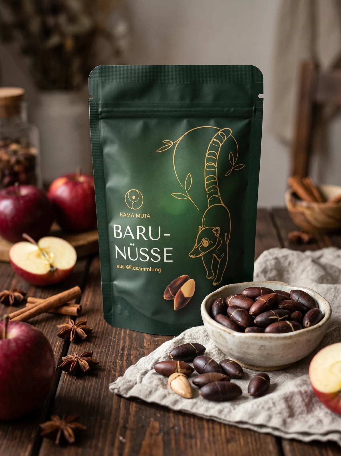 KAMA MUTA Baru-Nüsse 125 g auf einem Holztisch mit roten Äpfeln, Zimtstangen, Sternanis und einer Schale gerösteter Baru-Nüsse (KI-generiert)